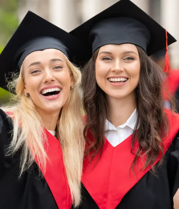 Two joyful female graduates in caps and gowns celebrating with diplomas outdoors.